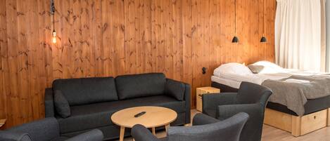 A modern room with a wooden wall, a sofa, two armchairs, a small round table, and a bed with a wooden headboard.