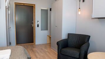A room with a dark grey armchair, a wooden floor, a wardrobe, and a small round table.