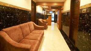 Un vestíbulo de hotel con una recepción, una sala de espera con sofás y un pasillo que conduce a los ascensores.