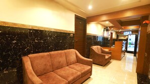 Un vestíbulo de hotel con un sofá y sillones, una recepción y una máquina expendedora.