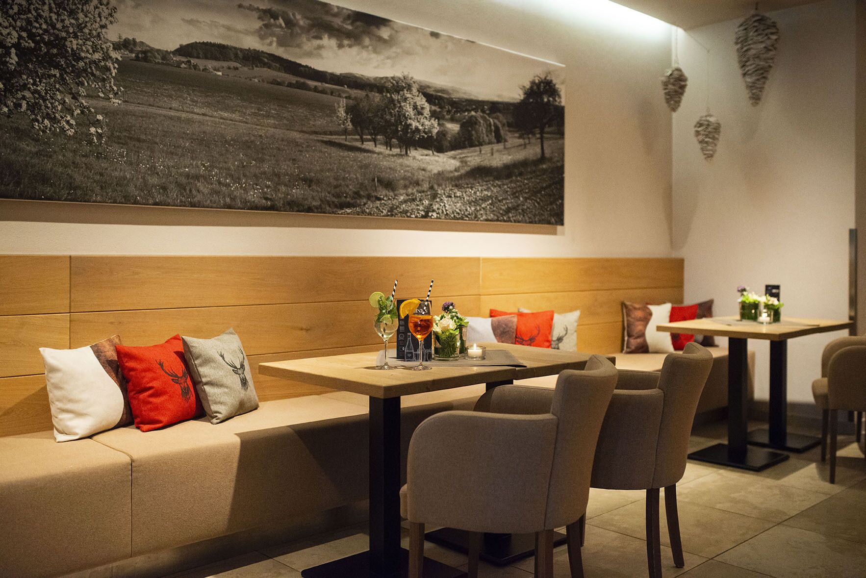 L'intérieur d'un restaurant moderne présente un coin salon avec un banc en bois, une table à manger avec des chaises, et un grand tableau représentant un paysage en noir et blanc accroché au mur.