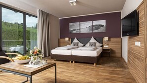 A modern bedroom with a large bed, a TV, and a dining area with a table set for two. - Müllers Landhotel (Mespelbrunn)