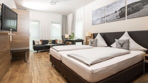 A modern hotel room with two beds, a sofa, a desk, and a TV. - Müllers Landhotel (Mespelbrunn)