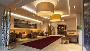 A modern hotel lobby with a dining area, a bar, and a seating area with a red carpet. - Müllers Landhotel (Mespelbrunn)