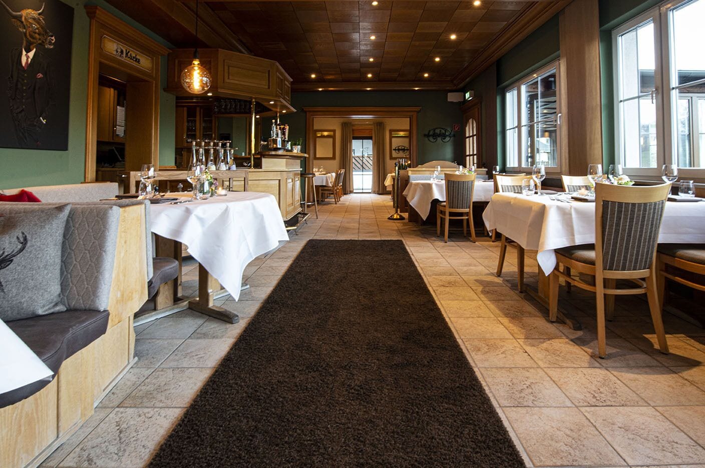 Ein Restaurant mit Holztischen, weißen Tischdecken und einem schwarzen Teppich.