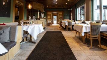 Ein Restaurant mit Holztischen, weißen Tischdecken und einem schwarzen Teppich.