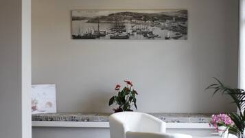 A room with a white chair, a small table, a potted plant, and a framed black and white photograph on the wall.