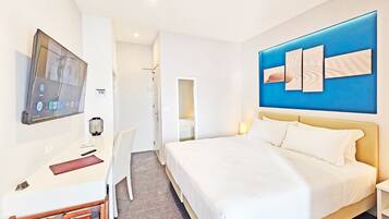 Ein modernes Hotelzimmer mit einem großen Bett, einem Schreibtisch mit Computer, einem an der Wand befestigten Fernseher und einer blauen Akzentwand.