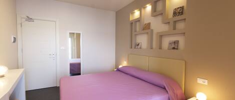 Un dormitorio con cama, mesita de noche y estante en la pared con fotografías.