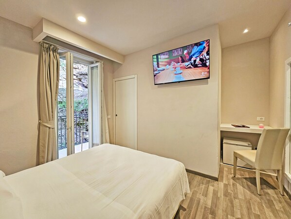 Habitación de hotel con cama, escritorio, silla, televisor y ventana con cortinas.