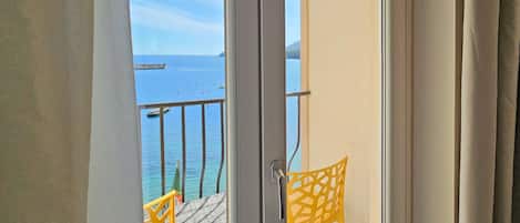 A balcony with a view of the sea, featuring two yellow chairs and a small table.