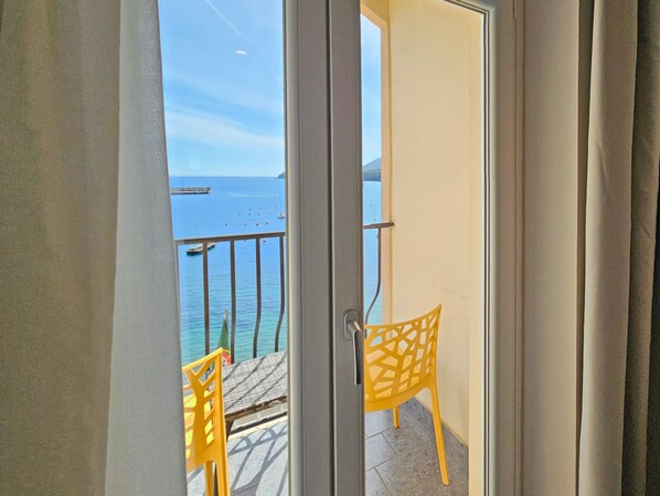 A balcony with a view of the sea, featuring two yellow chairs and a small table.