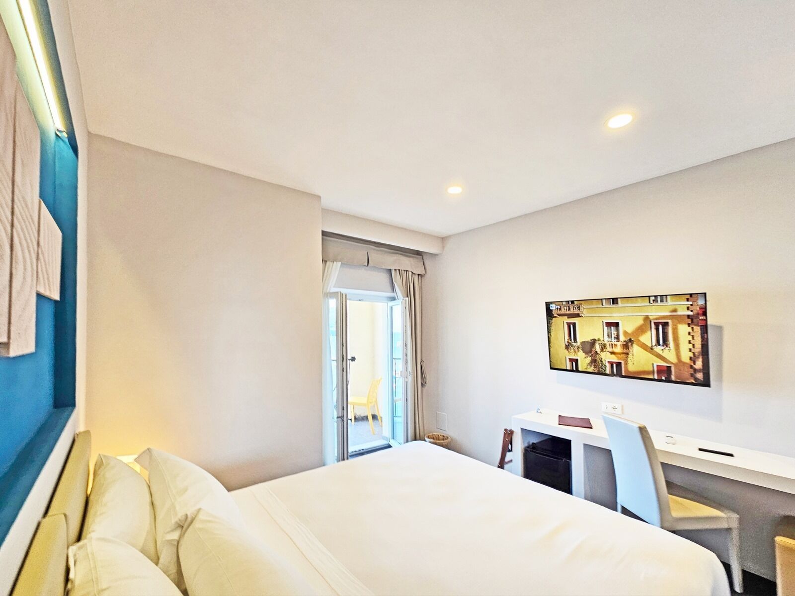 Una camera d'albergo con un letto, una scrivania, una sedia e una televisione appesa al muro.