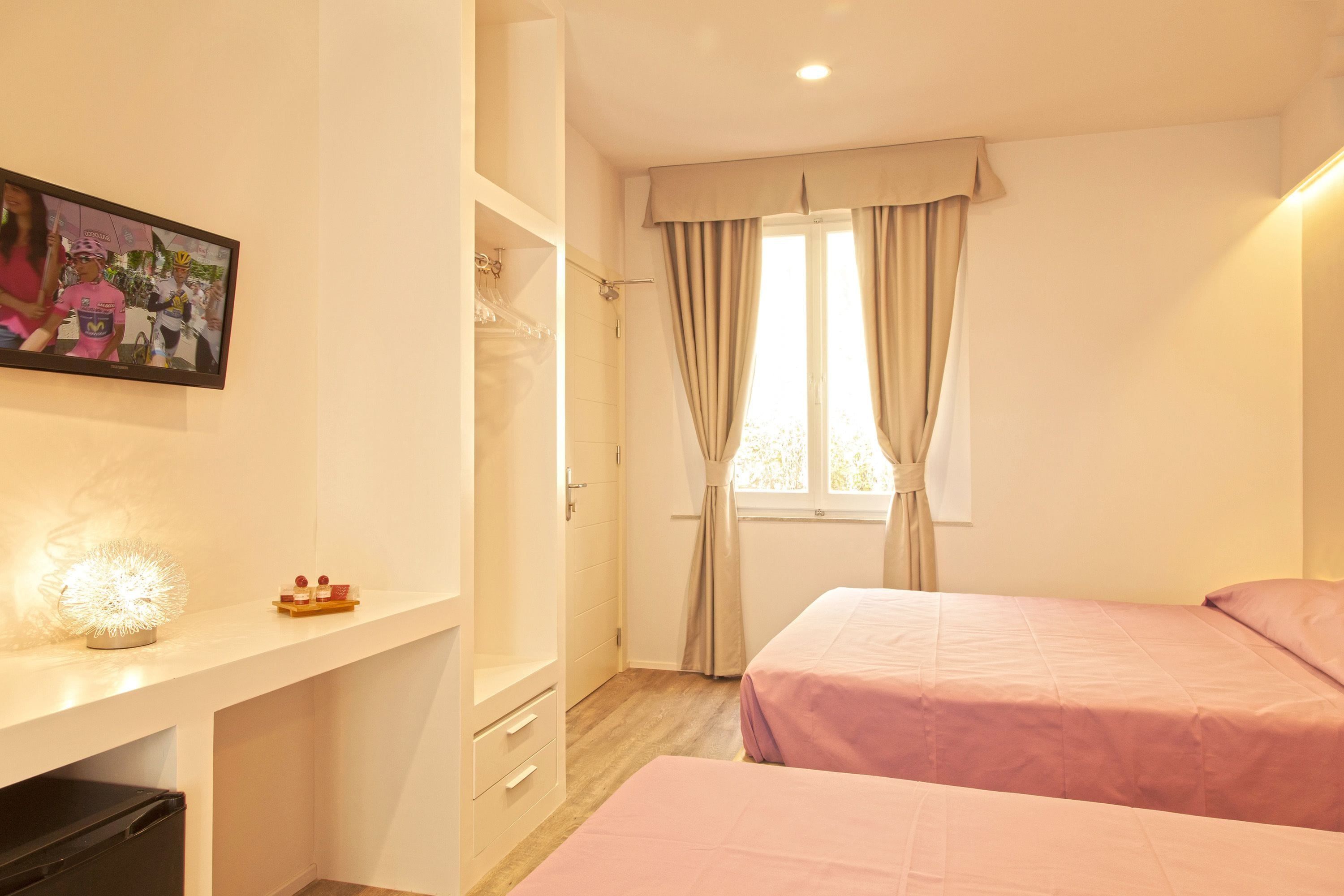 A bedroom with two beds, a wardrobe, a desk, and a window with curtains.