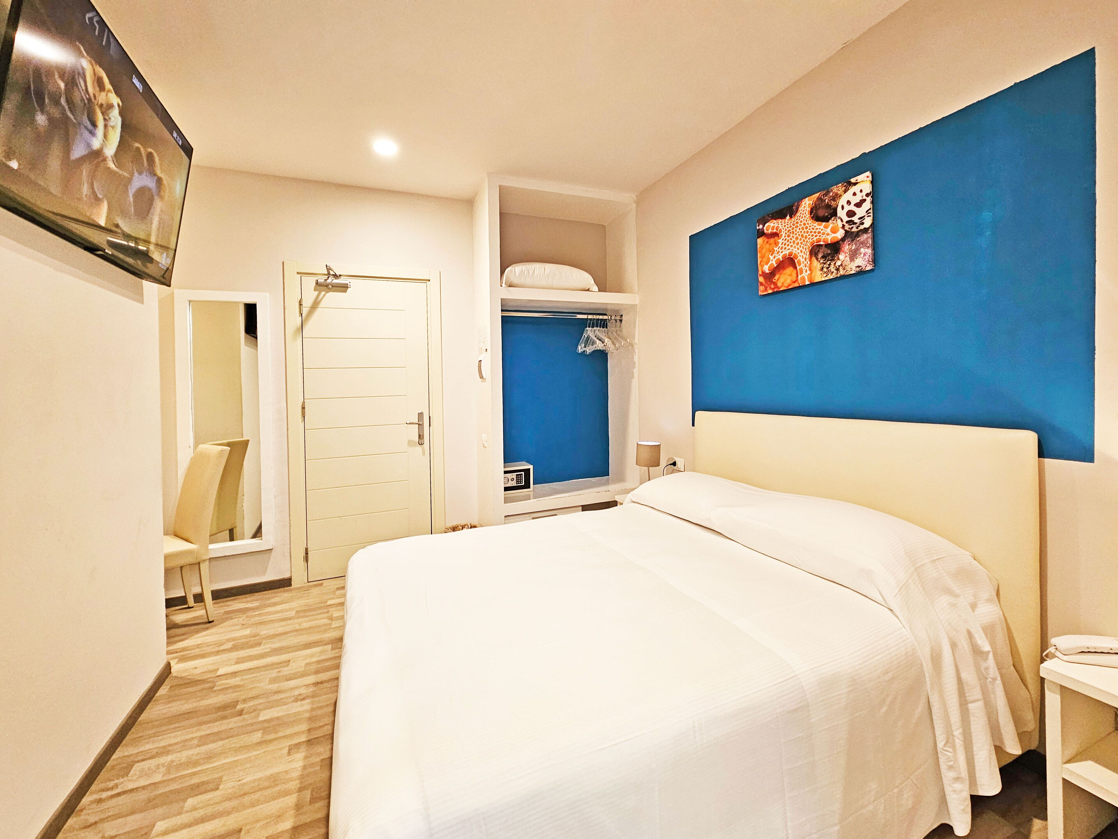 A hotel room with a bed, a TV, a wardrobe, and a blue accent wall.