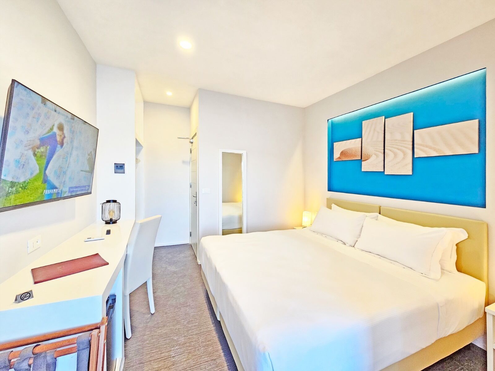 A hotel room with a bed, a desk, a chair, and a TV mounted on the wall.