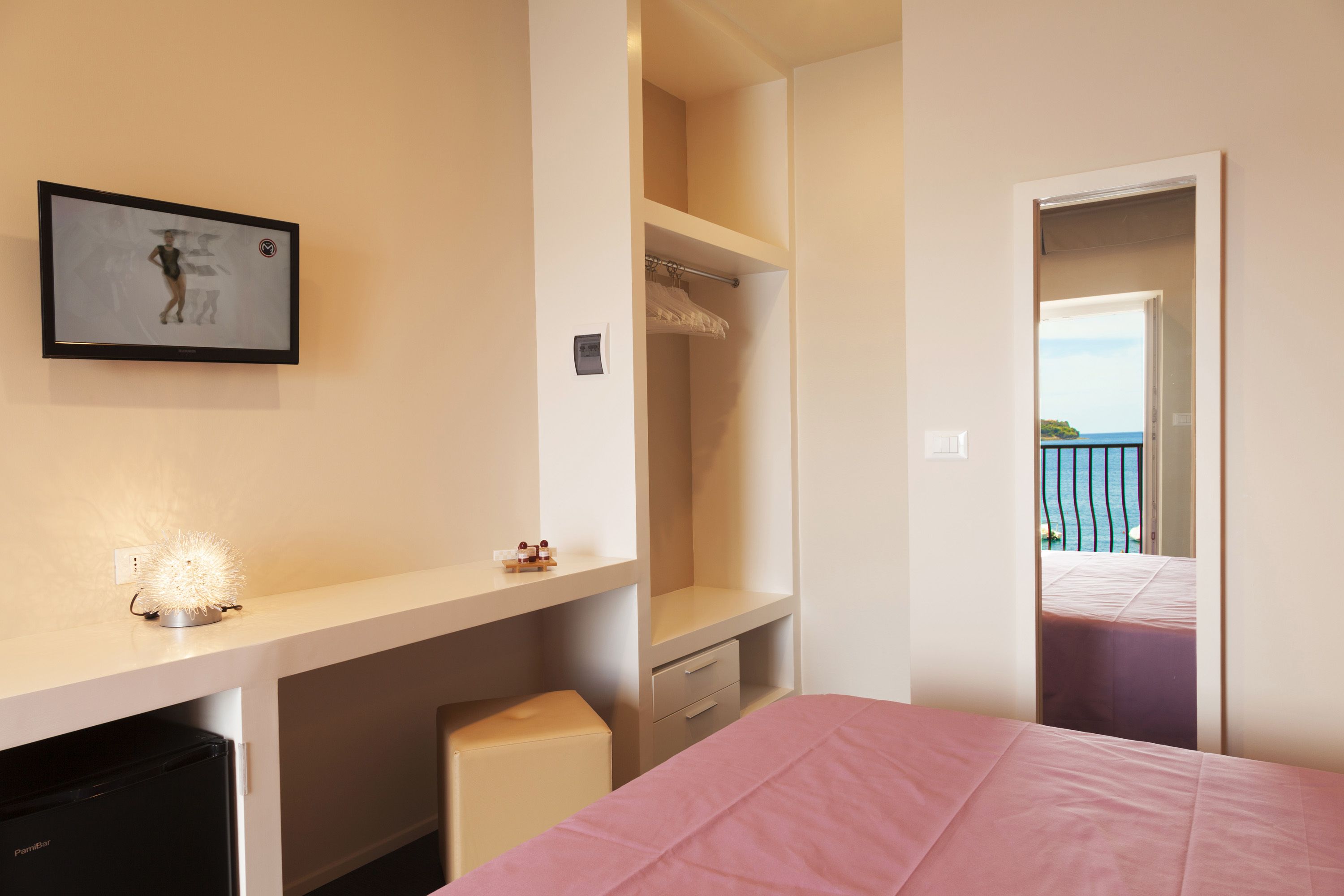 A bedroom with a bed, a desk, a wardrobe, and a view of the sea through an open door.