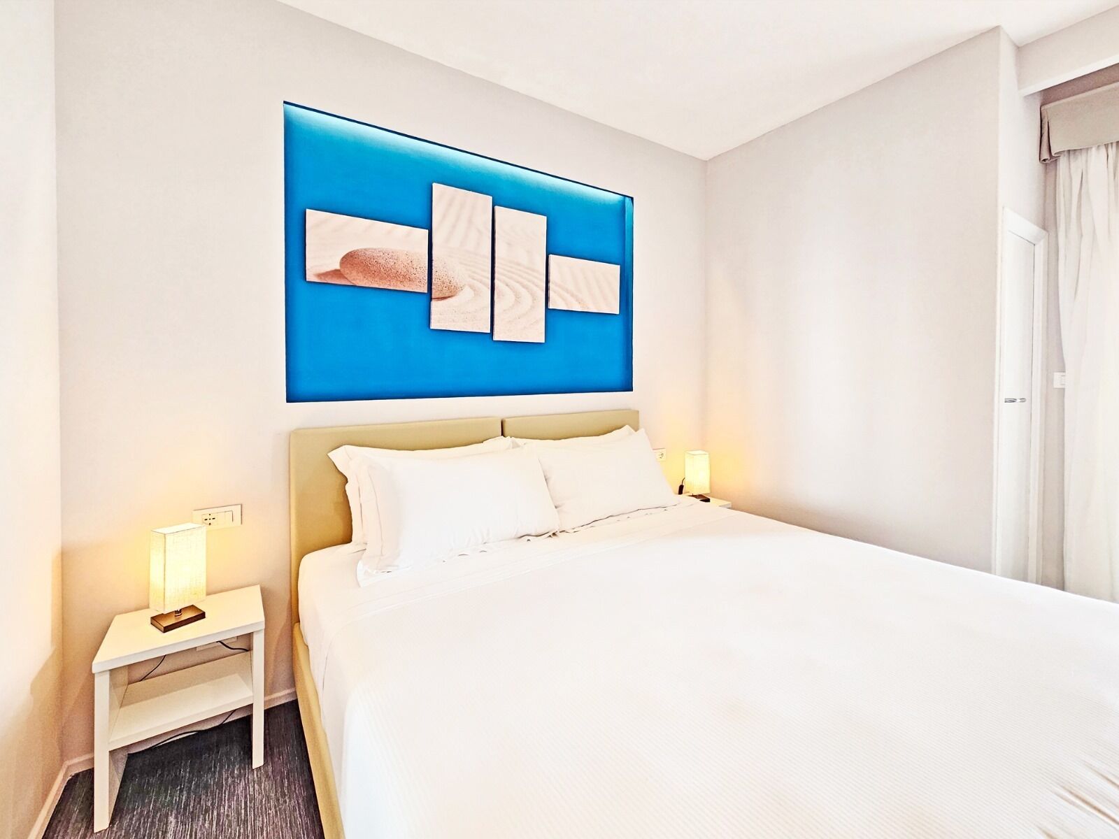 Una habitación de hotel con una cama grande, dos mesitas de noche y una pared decorada en azul.