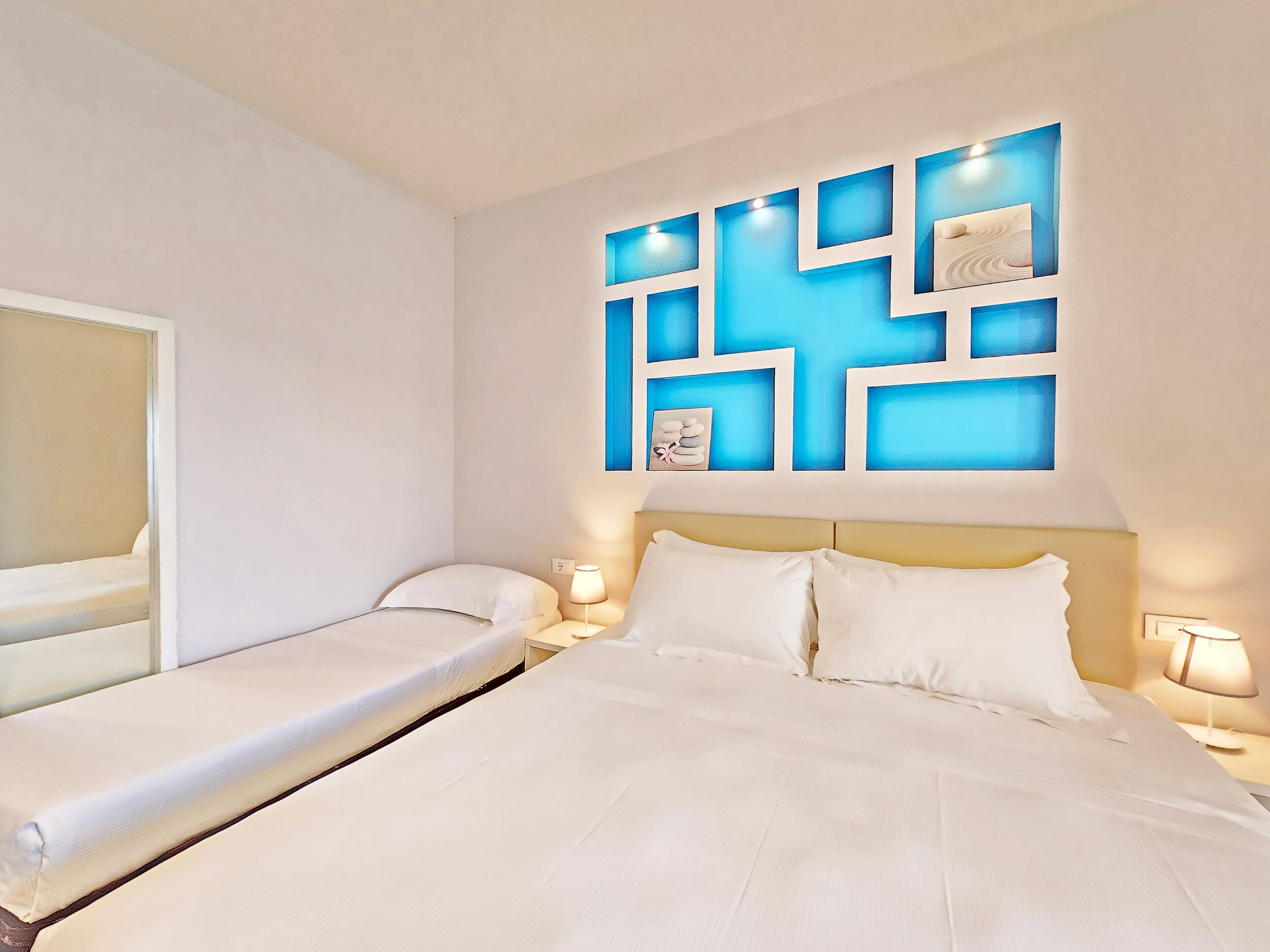 A hotel room with a large bed, a smaller bed, two bedside tables, and a wall with a geometric light fixture.