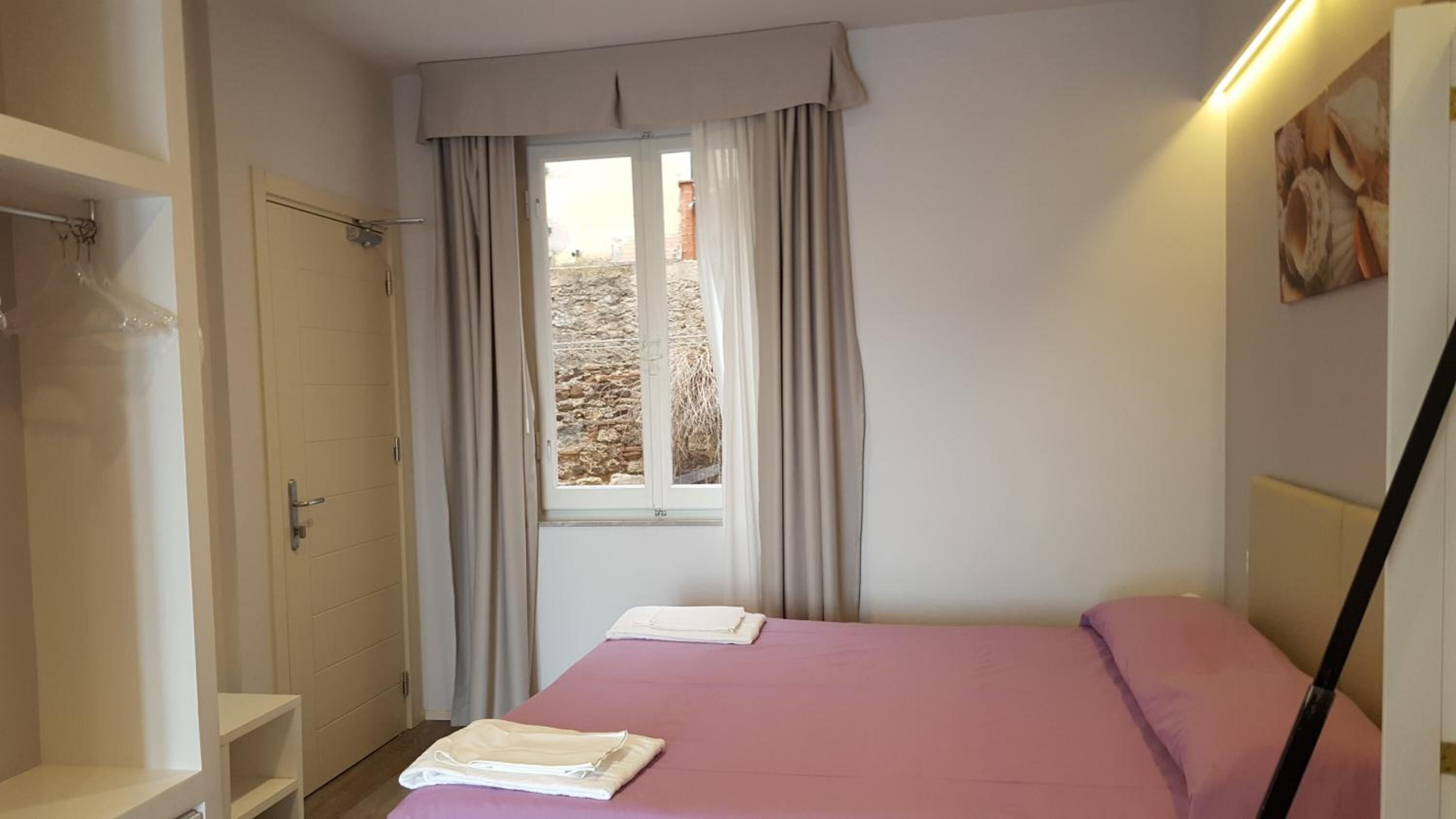 Ein Schlafzimmer mit einem Bett, einem Fenster mit Vorhängen, einem Kleiderschrank und einem Handtuch auf dem Bett.