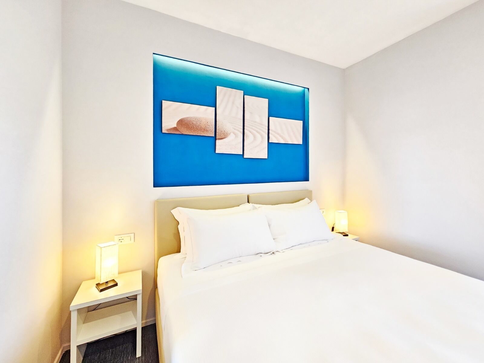 Una habitación de hotel con una cama, dos mesitas de noche y una obra de arte colgada en la pared.