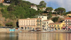 Un pueblo costero con edificios a lo largo de la costa, barcos amarrados y una colina con árboles.