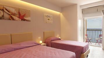 A hotel room with two beds, a large window with a view of the sea, and a balcony with chairs.