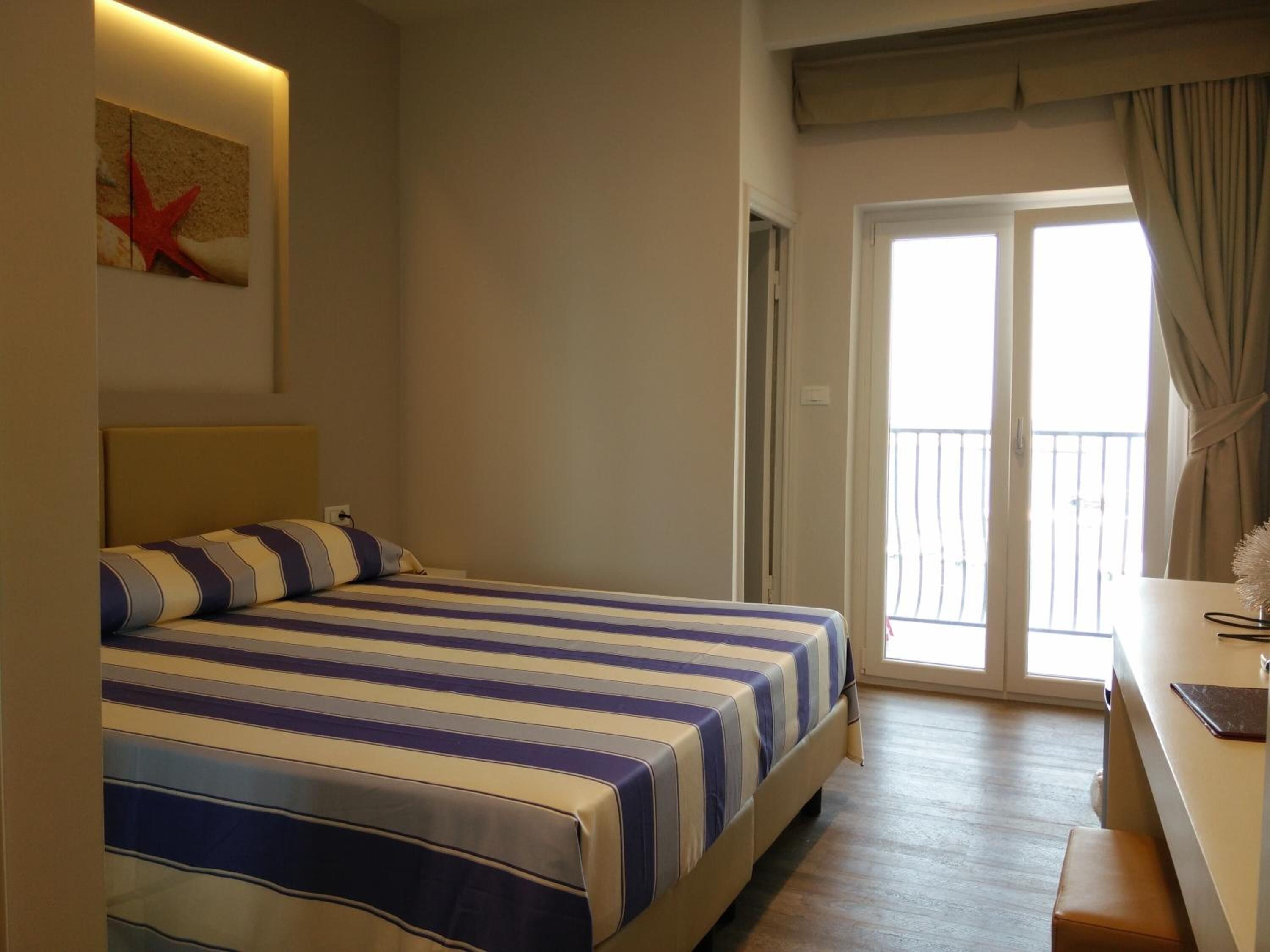A hotel room with a bed, a desk, a chair, a window with curtains, and a starfish decoration on the wall.