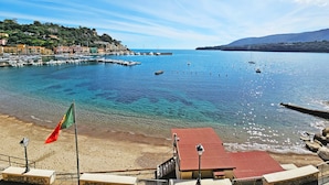 Un pueblo costero con un puerto deportivo, aguas azules cristalinas y una playa de arena.