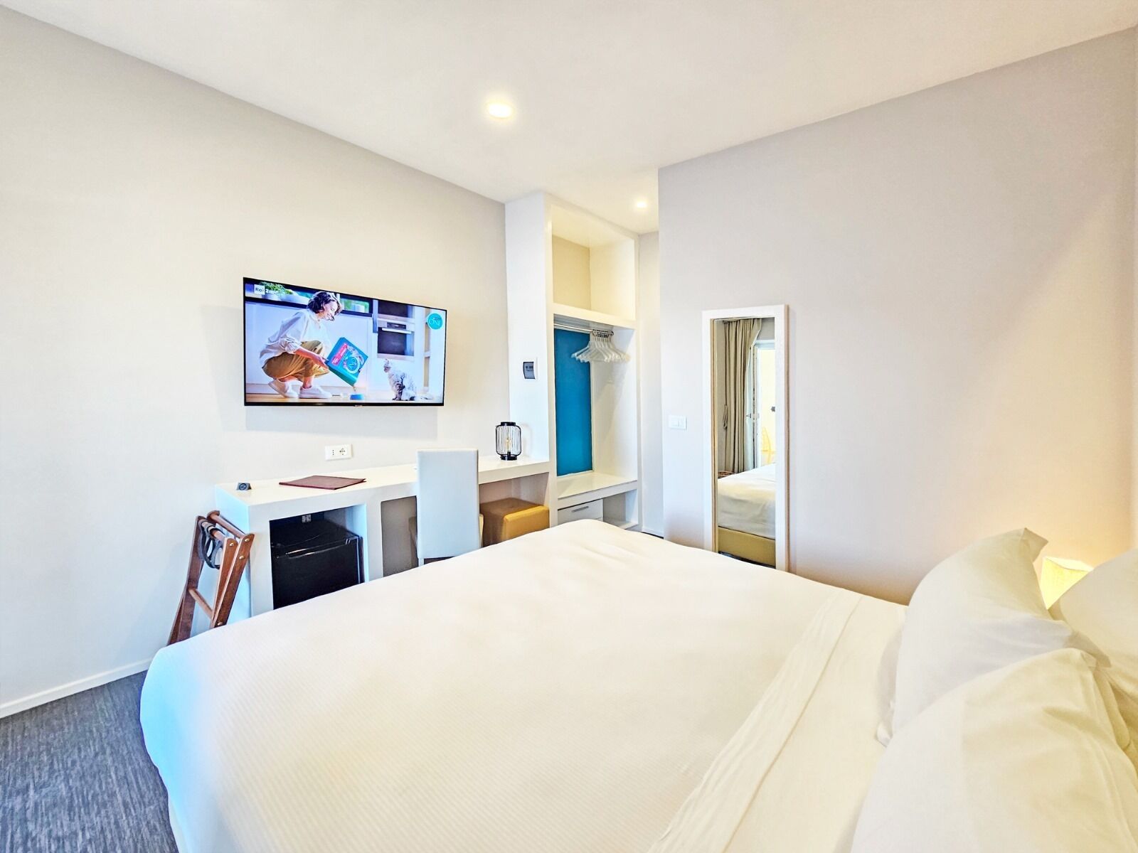 A hotel room with a bed, a desk with a chair, a television mounted on the wall, and a wardrobe.