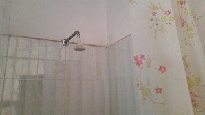 A shower with a handheld showerhead in a room with tiled walls and floral wallpaper. - St. Gotthard Motel Bar & Restaurant (Malindi)