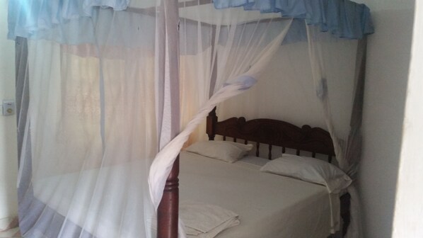 Una cama con cabecera de madera, ropa de cama blanca y dosel blanco.