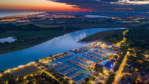 An aerial view of a marina with numerous boats docked, surrounded by residential buildings and a river. - Floating Resort (Lignano Sabbiadoro)