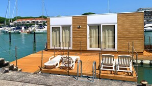 A modern yacht with a wooden deck, lounge chairs, and a glass-enclosed cabin with curtains. - Floating Resort (Lignano Sabbiadoro)
