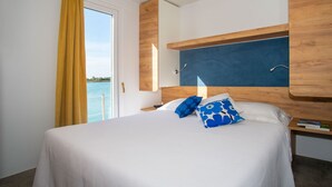 A hotel room with a bed, a wooden headboard, a nightstand, and a view of the sea. - Floating Resort (Lignano Sabbiadoro)