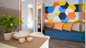 A modern living room with a blue sofa, decorative pillows, a potted plant, and a geometric-patterned wall. - Floating Resort (Lignano Sabbiadoro)