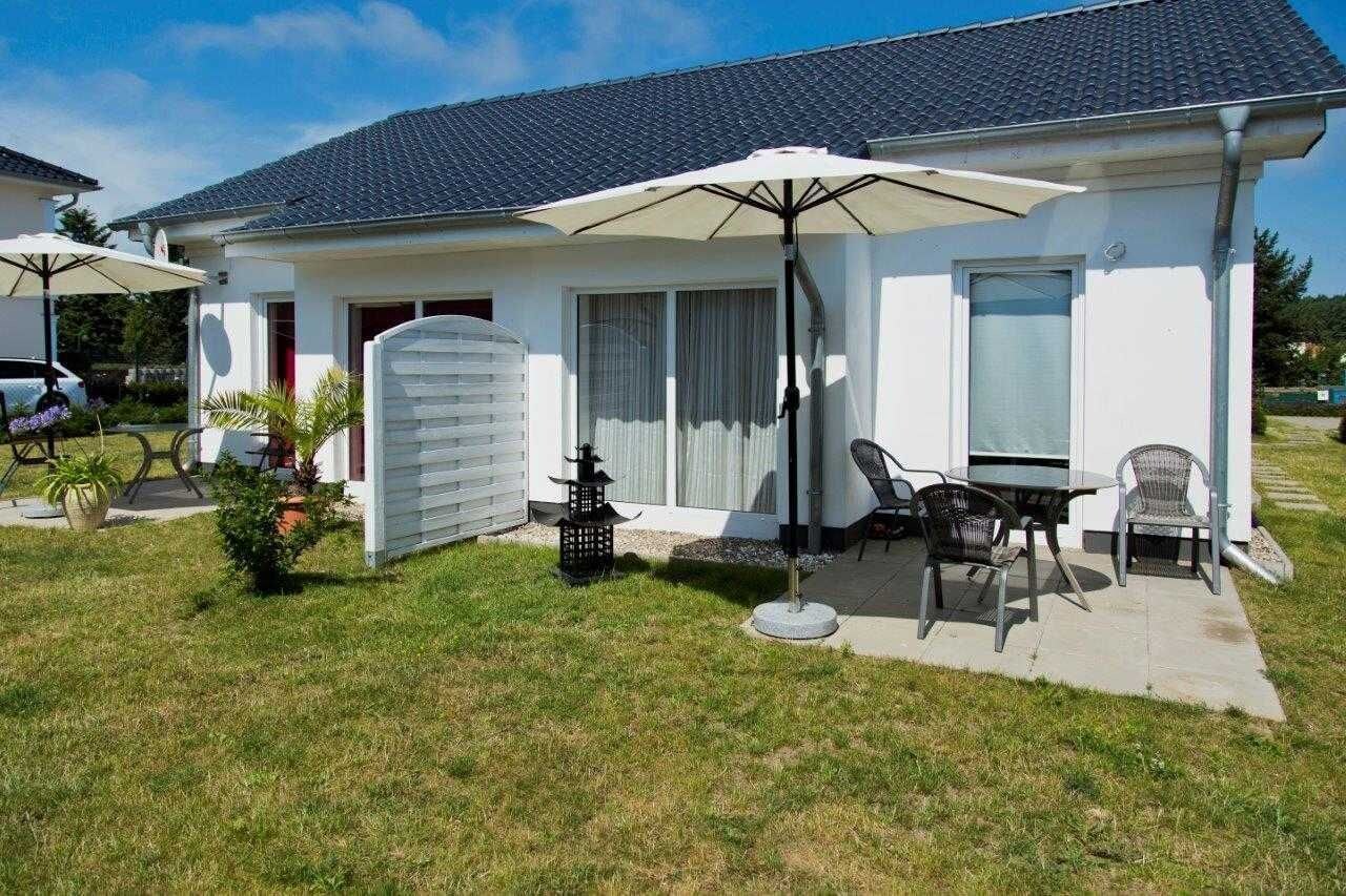 Einbungalow mit Terrasse, der mit Gartenmöbeln und einem großen Sonnenschirm ausgestattet ist.