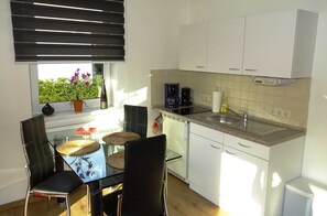 A compact kitchen with a dining area, featuring a glass table, black chairs, a potted plant, a coffee maker, and a built-in oven. - Vacation apartment 2 - Ück - Rolletschke Andreas (Ückeritz)