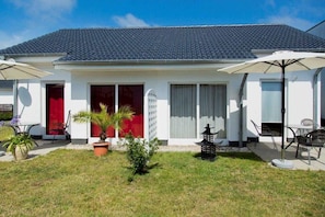 A two-story house with a tiled roof, a red door, and a small garden with potted plants and a lantern. - Vacation apartment 2 - Ück - Rolletschke Andreas (Ückeritz)