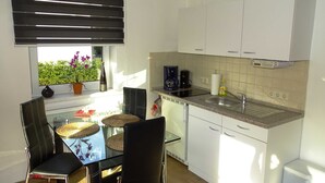 A compact kitchen with a dining area, featuring a glass table, black chairs, a potted plant, a coffee maker, and a built-in oven. - Vacation apartment 2 - Ück - Rolletschke Andreas (Ückeritz)