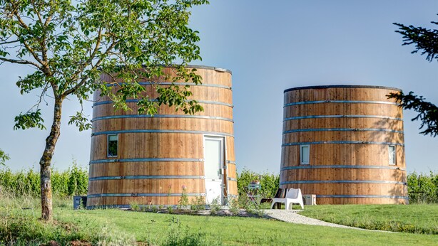 Two cylindrical wooden structures with windows, surrounded by a grassy area with a tree and a white chair. - Coup 2 Foudres (Saint-Jean-de-Blaignac)