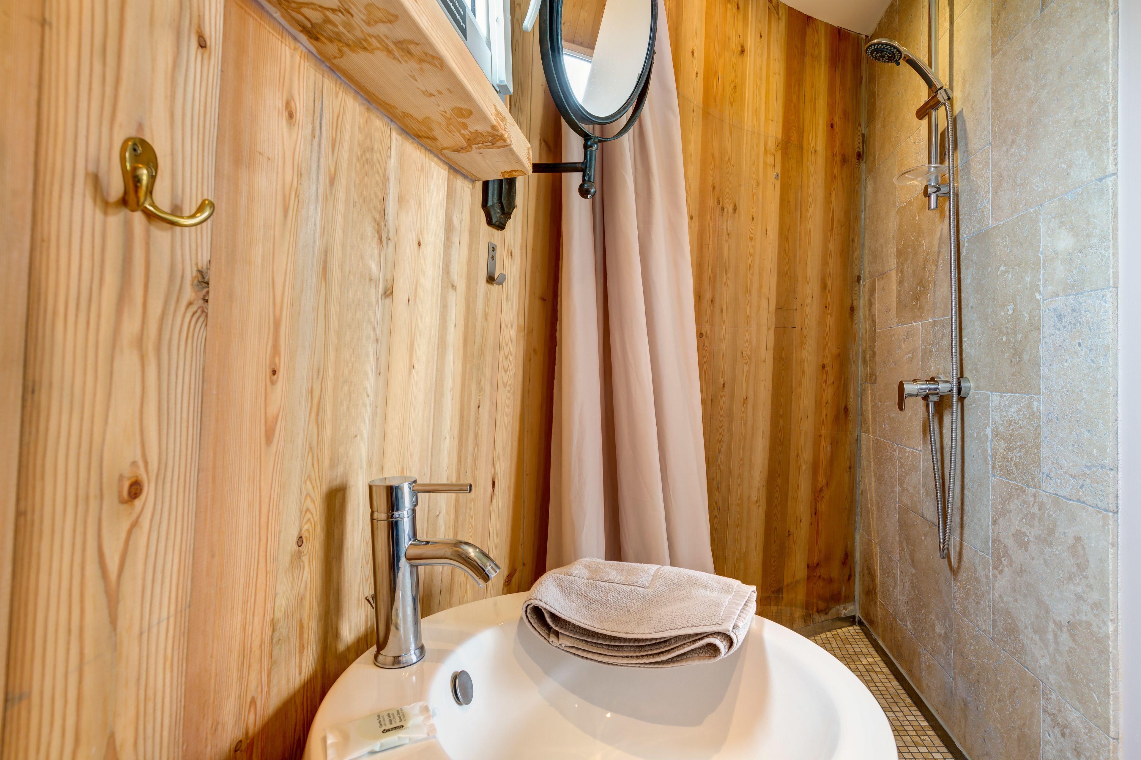 A wooden interior bathroom with a sink, mirror, and shower.