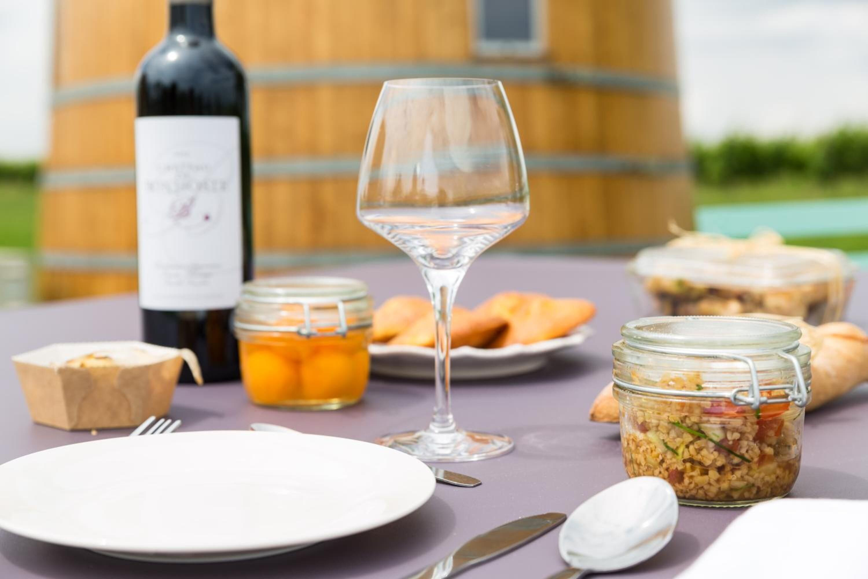 Uma mesa com uma garrafa de vinho, uma taça, potes de comida e um prato.