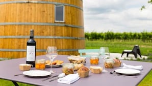 A table set outdoors with food and drinks, a wine bottle, and a wooden barrel in the background. - Coup 2 Foudres (Saint-Jean-de-Blaignac)
