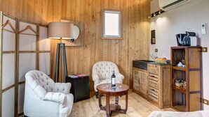 A cozy room with a wooden ceiling, a round wooden table with a bottle and glasses, a white armchair, a sofa, a small black fridge, a wooden cabinet, and a window with a view. - Coup 2 Foudres (Saint-Jean-de-Blaignac)