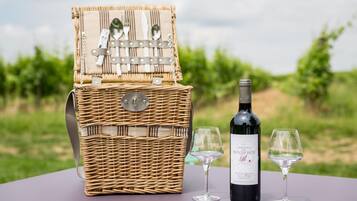 A wicker picnic basket with a wine bottle and two glasses on a table with a vineyard in the background.
