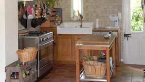 Une cuisine rustique avec une cuisinière à gaz, des armoires en bois, un dosseret carrelé et une petite table à manger.
