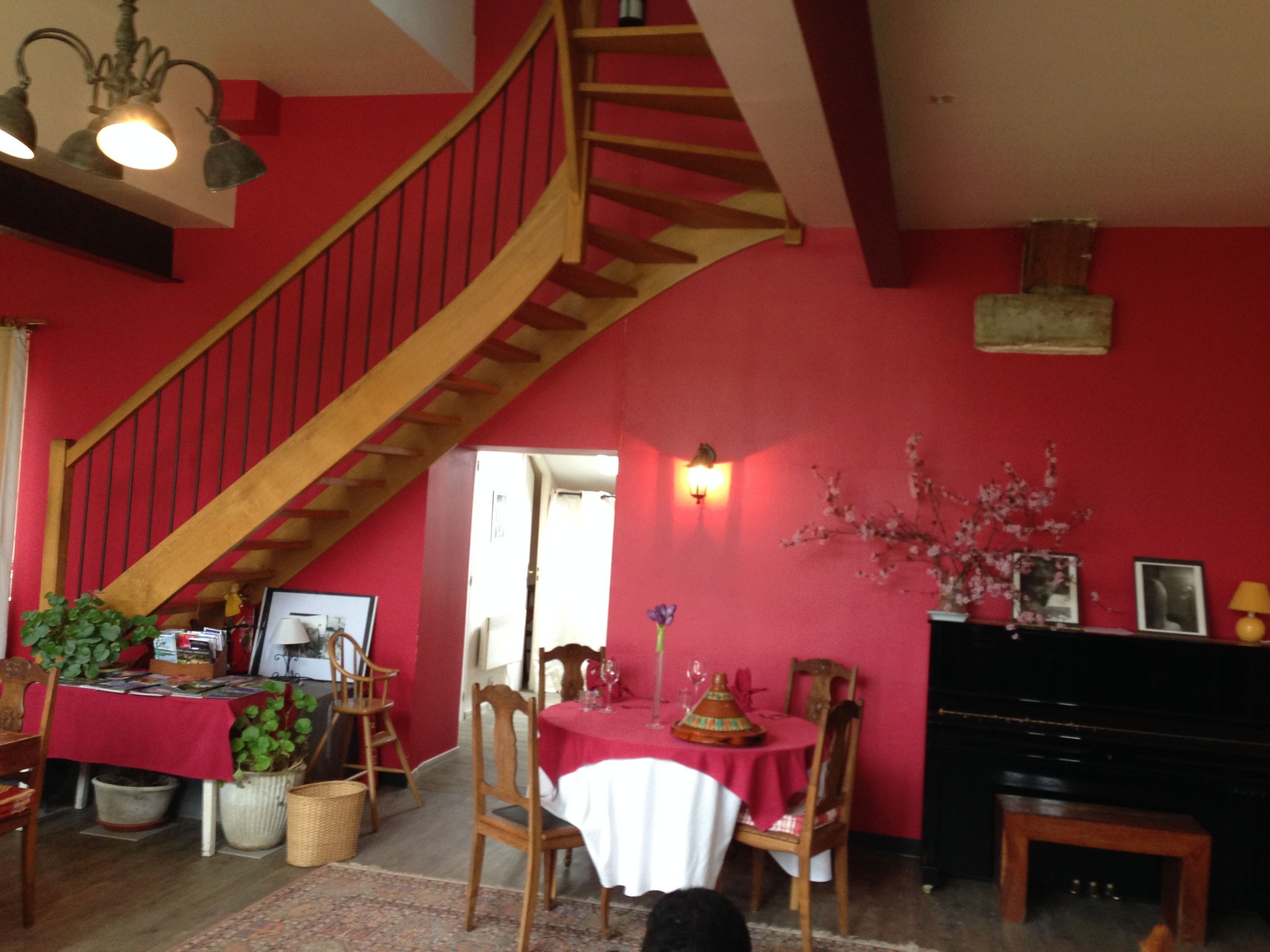 Un comedor con pared roja, escalera de madera, mesa de comedor con sillas y un piano.