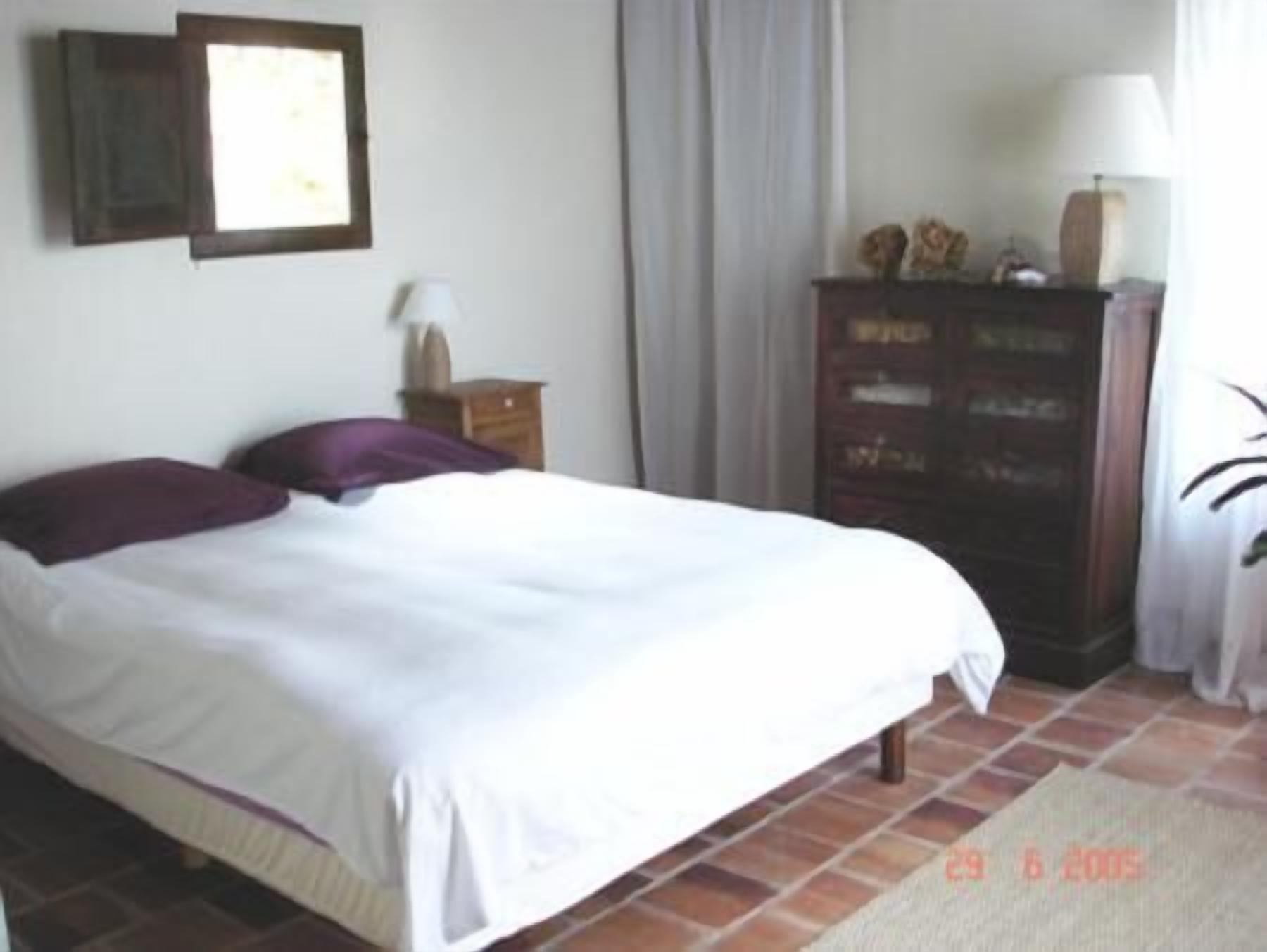 Un dormitorio con cama, cómoda, mesita de noche y ventana con cortinas.