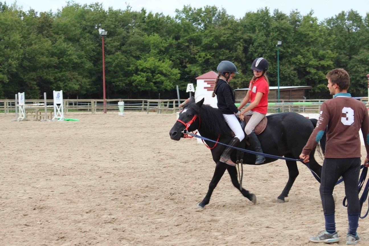 Een persoon die op een paard rijdt in een openbare arena met een zandbodem, omringd door een hek en bomen op de achtergrond.